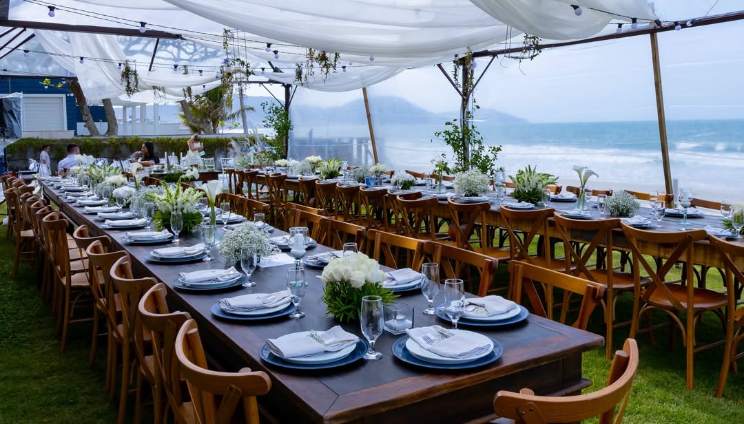 Mesas longas à beira-mar com decoração floral branca